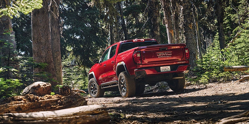 Back view of a 2024 GMC Canyon driving on a dirt road through a forest