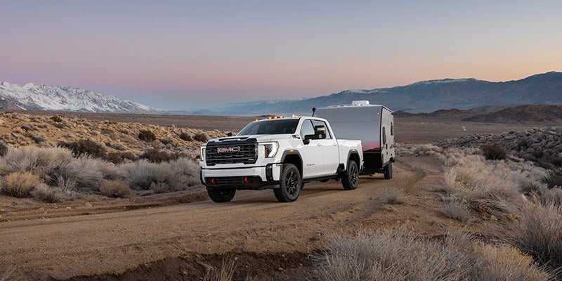 2024 GMC Sierra 2500HD driving on a dirt road with snowy mountains in the background