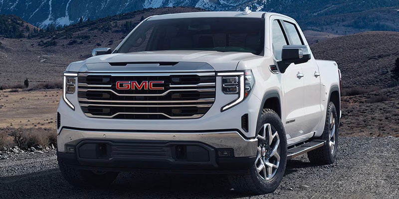 2025 GMC Sierra 1500 AT4X in the color white on top of a road with small rocks with snowy mountains in the background