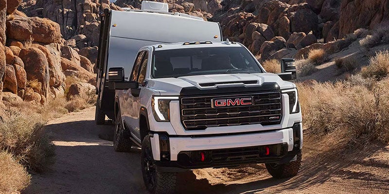 2025 GMC Sierra 3500HD towing a trailer on a hilly dirt terrain